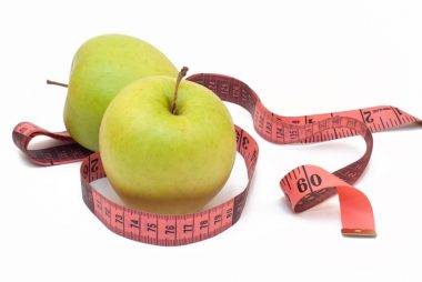 two green apples with a measuring tape around them